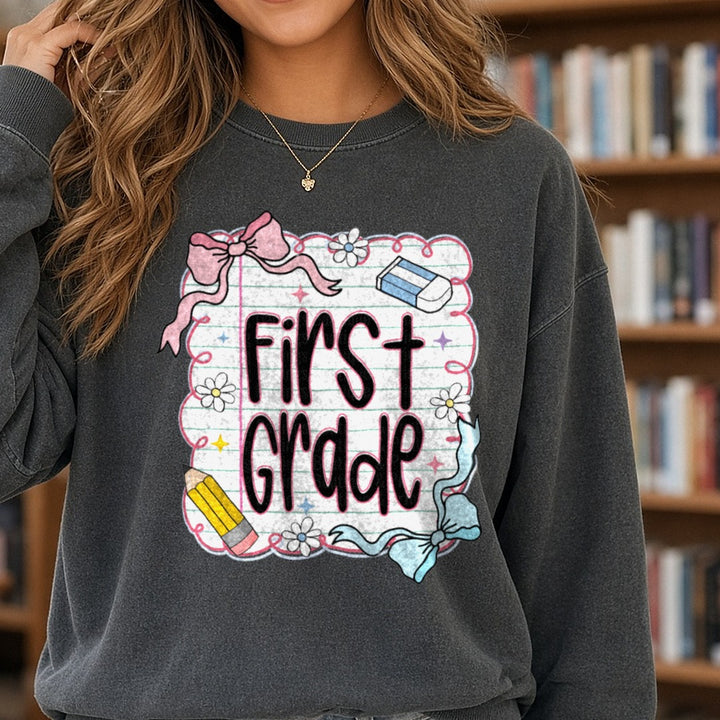 First Grade Notebook Paper Pink Bow Pencil DTF transfer shown on a Comfort Colors sweatshirt