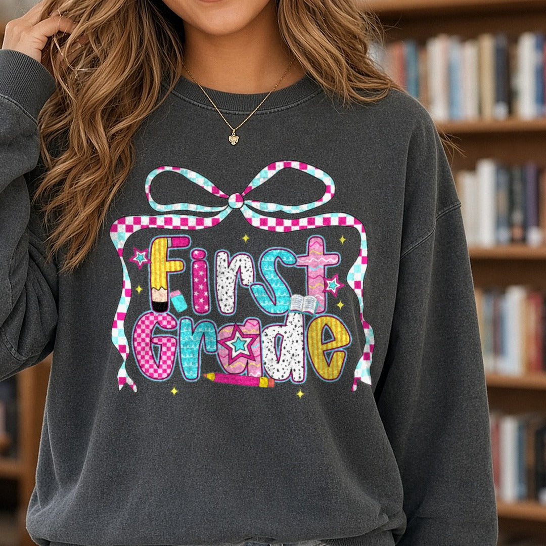 First Grade Checkered Ribbon Bow Patterned Letters DTF transfer shown on a Comfort Colors sweatshirt