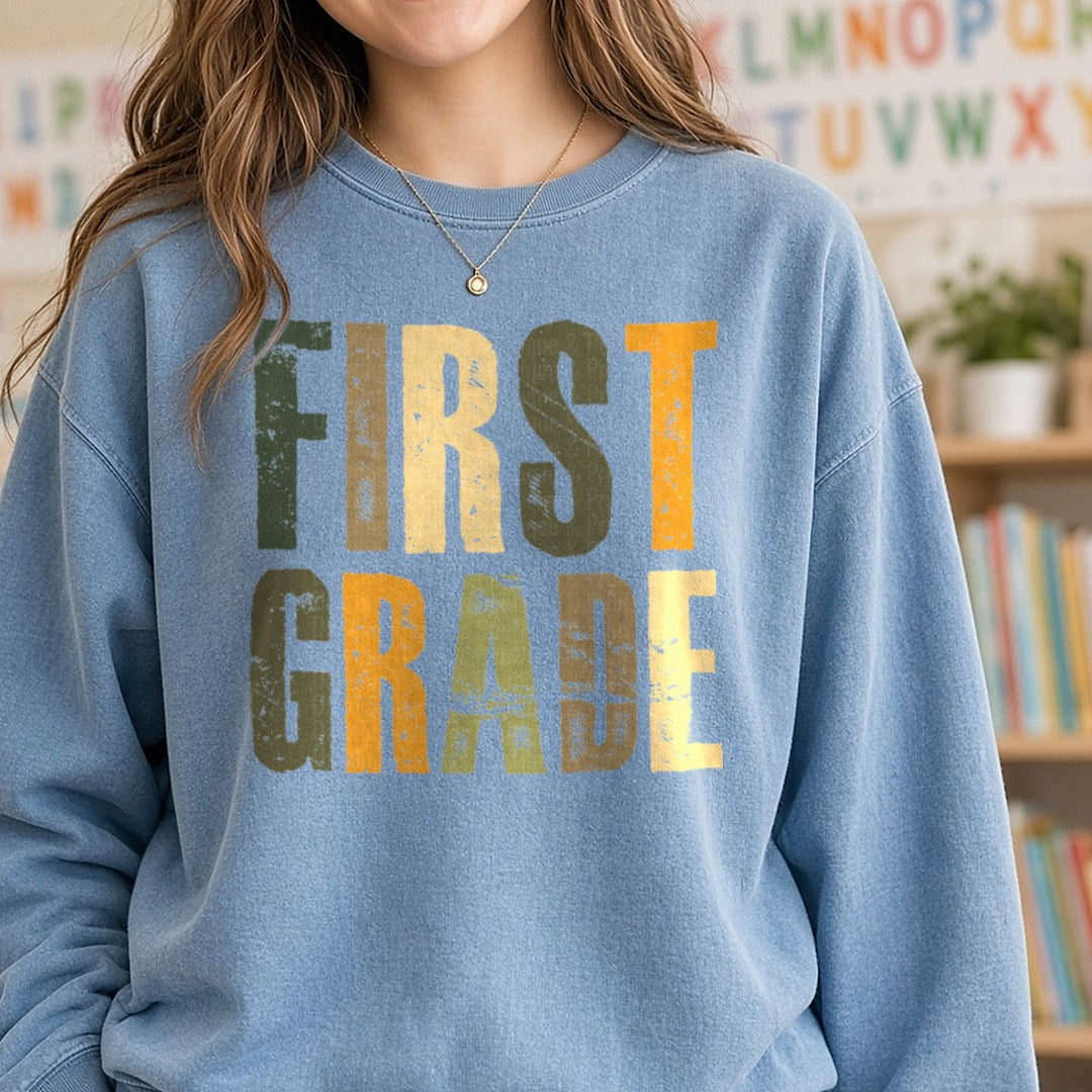 First Grade Distressed Green Orange Block Letters DTF transfer shown on a Comfort Colors sweatshirt
