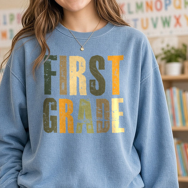 First Grade Distressed Green Orange Block Letters DTF transfer shown on a Comfort Colors sweatshirt