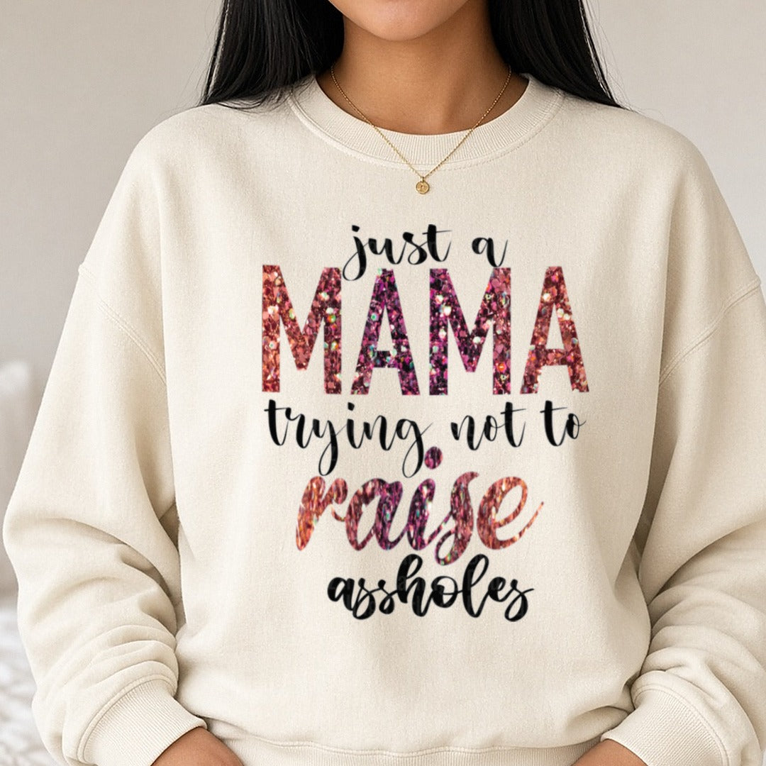 Just A Mama Trying Not To Raise A**holes Glitter DTF transfer shown on a Comfort Colors sweatshirt