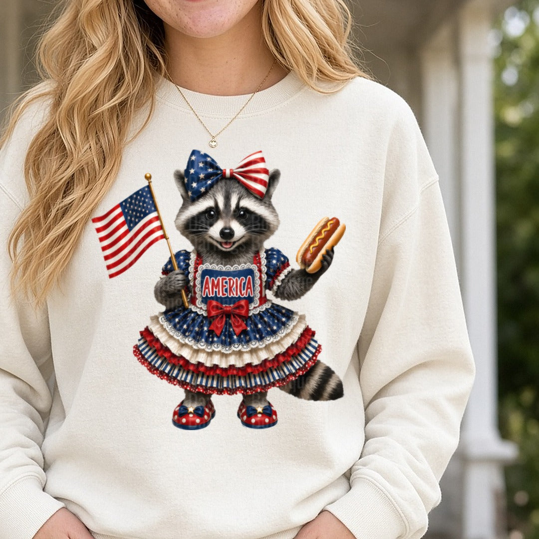 Patriotic Raccoon in American Flag Dress Holding Hot Dog and Flag DTF transfer shown on a Comfort Colors sweatshirt