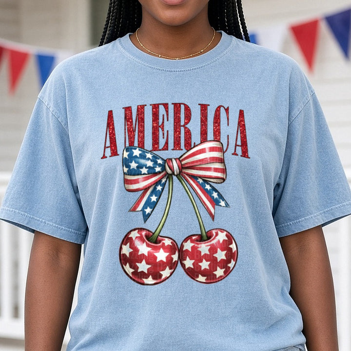 America Glitter Text Patriotic Cherries Stars and Stripes Bow DTF transfer shown on a Comfort Colors tee