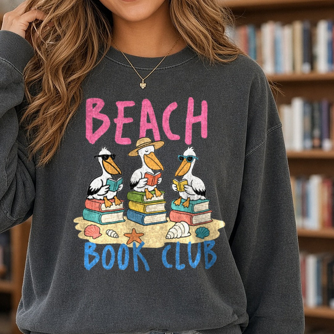 Beach Book Club Pelicans Reading on Sand with Seashells DTF transfer shown on a Comfort Colors sweatshirt