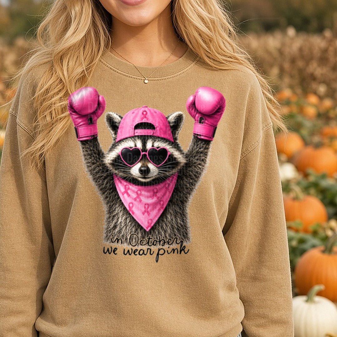 Raccoon Boxing Gloves Pink Ribbon In October We Wear Pink Black Script DTF transfer shown on a Comfort Colors sweatshirt