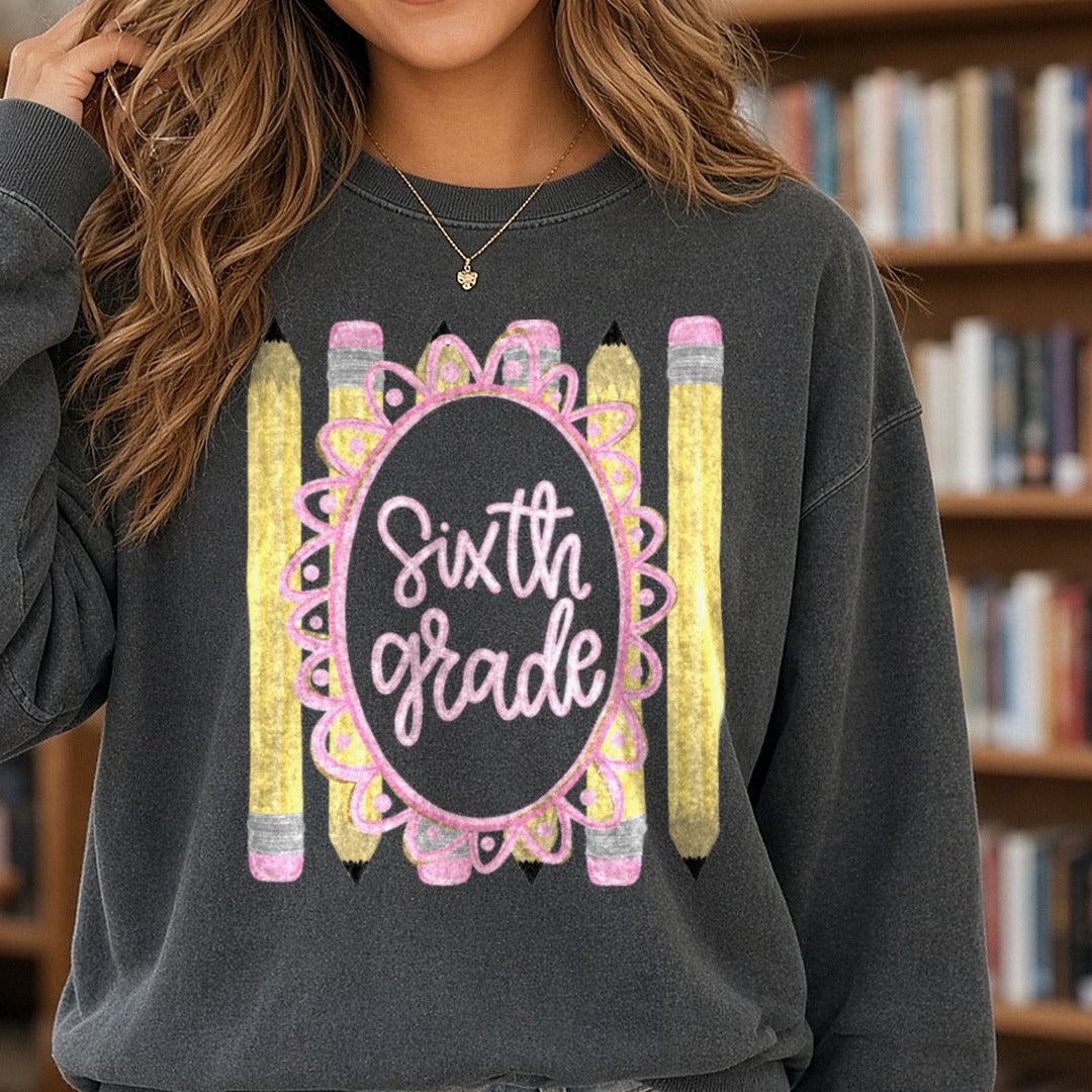 Sixth Grade Pink Script Oval Frame with Yellow Pencils DTF transfer shown on a Comfort Colors sweatshirt